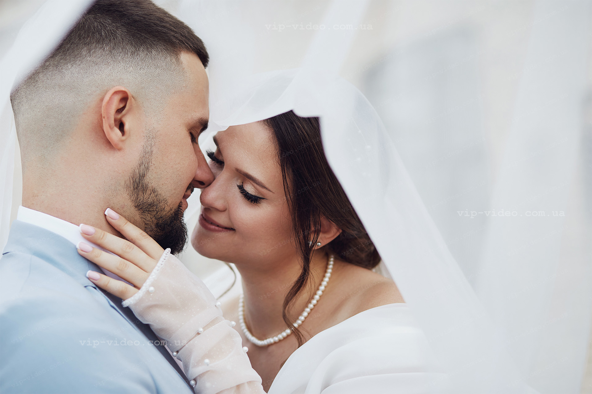 Фотографія з весілля на якій молодята ніжно доторкаються головами один до одного на фоні білої фати нареченої